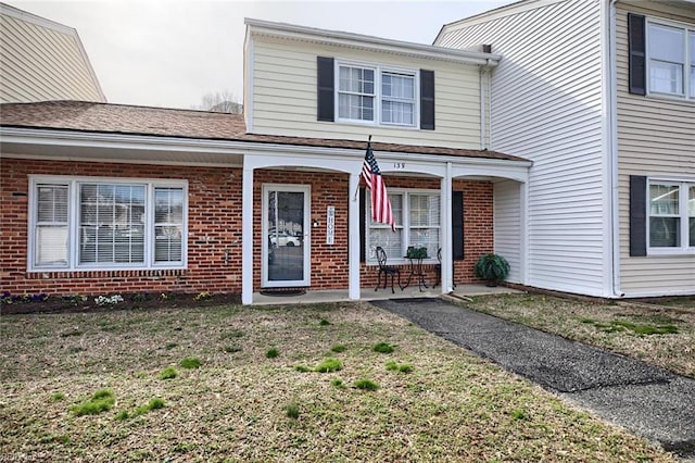 view of front of property with a front lawn, covered porch, and brick siding