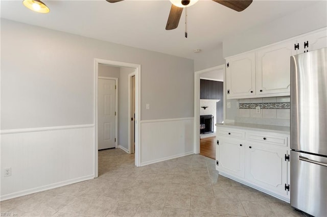 kitchen with a wainscoted wall, a ceiling fan, freestanding refrigerator, white cabinets, and light countertops