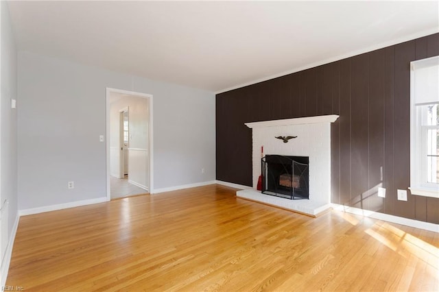 unfurnished living room with baseboards, wooden walls, a fireplace, and light wood finished floors