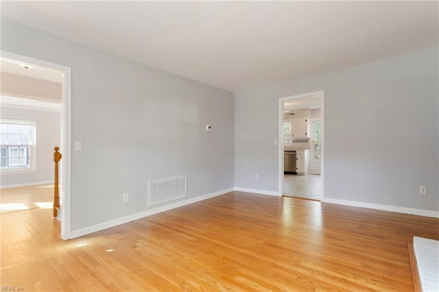 unfurnished room with a healthy amount of sunlight, visible vents, light wood finished floors, and baseboards