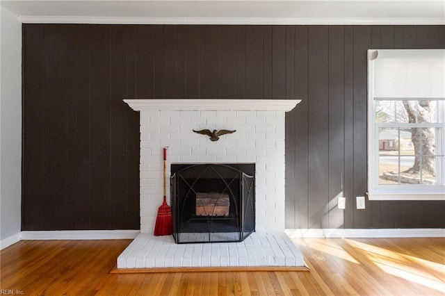 room details featuring ornamental molding, wood finished floors, wood walls, baseboards, and a brick fireplace