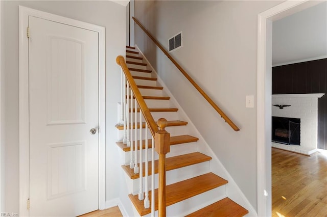 stairway featuring visible vents, a brick fireplace, baseboards, and wood finished floors