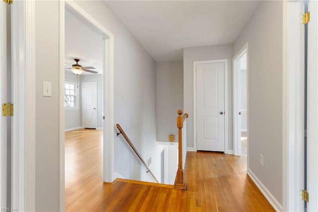 hall with baseboards, an upstairs landing, and light wood finished floors