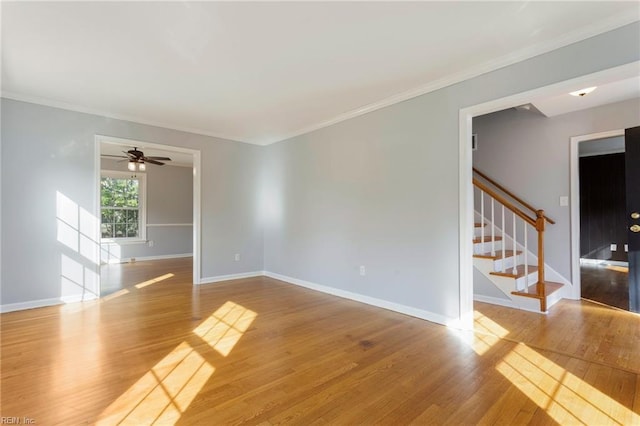 empty room featuring baseboards, wood finished floors, stairs, and crown molding