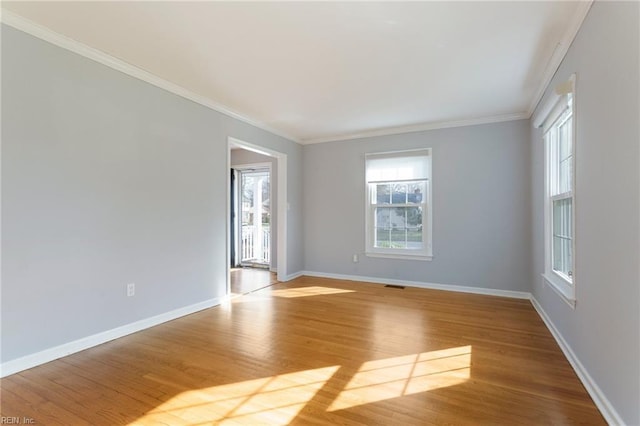 empty room with crown molding, visible vents, baseboards, and light wood finished floors