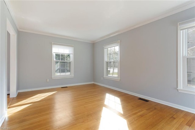 empty room with light wood-type flooring, visible vents, baseboards, and crown molding