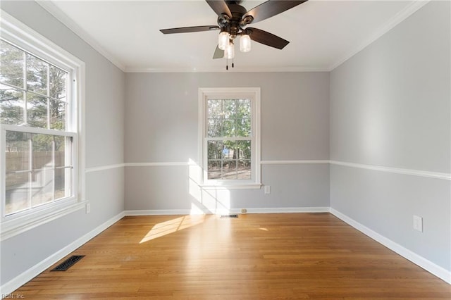 empty room featuring crown molding, wood finished floors, visible vents, and baseboards