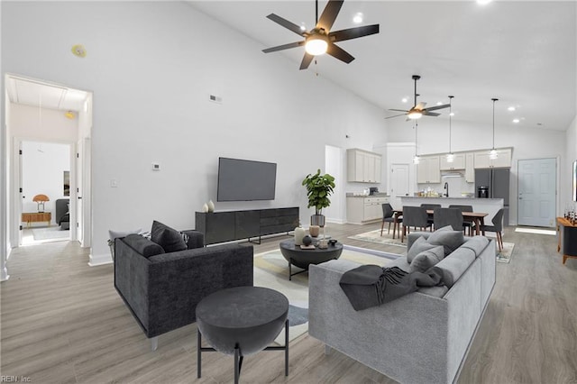 living area with a ceiling fan, visible vents, high vaulted ceiling, attic access, and light wood-style floors