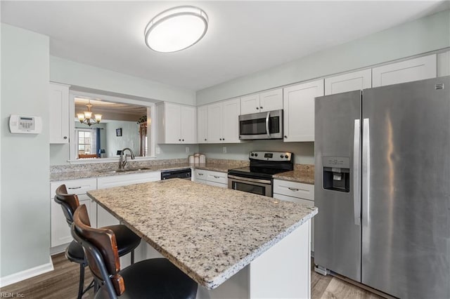 kitchen with wood finished floors, a kitchen island, a sink, appliances with stainless steel finishes, and white cabinetry