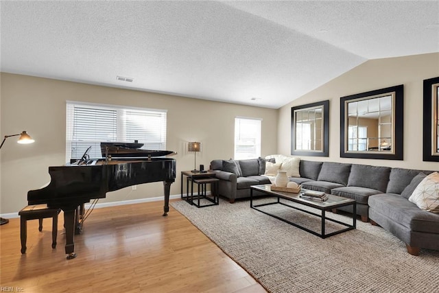 living area featuring visible vents, baseboards, vaulted ceiling, light wood-style flooring, and a textured ceiling