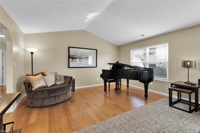 sitting room featuring vaulted ceiling, arched walkways, light wood finished floors, and a textured ceiling