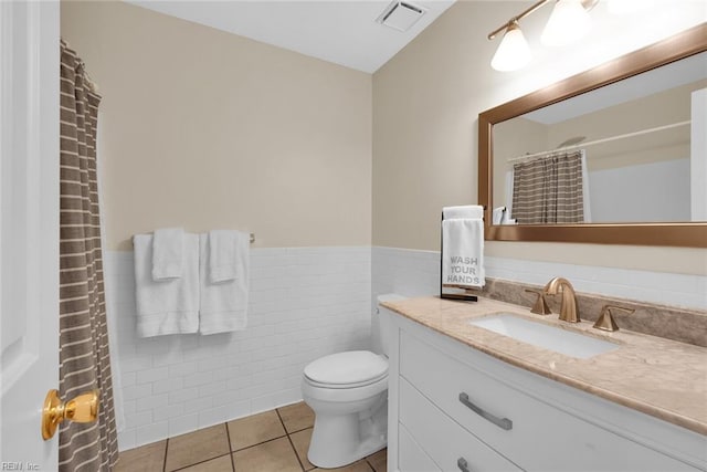 bathroom featuring tile patterned flooring, visible vents, vanity, wainscoting, and tile walls