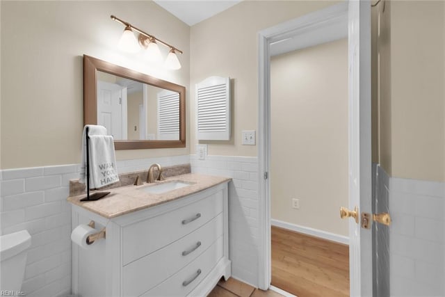 half bathroom featuring a wainscoted wall, toilet, vanity, wood finished floors, and tile walls