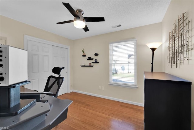 office featuring baseboards, visible vents, light wood finished floors, and a textured ceiling