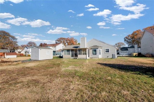 back of property featuring a lawn, a shed, an outdoor structure, a sunroom, and a chimney