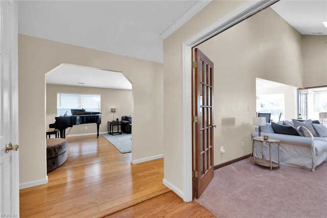 corridor featuring light wood-style flooring, baseboards, arched walkways, and a towering ceiling