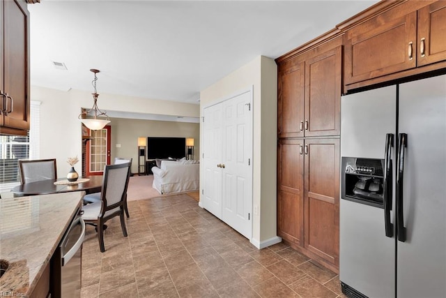 kitchen with visible vents, light stone countertops, decorative light fixtures, open floor plan, and stainless steel fridge with ice dispenser