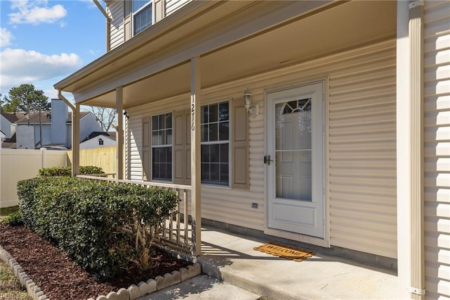 view of exterior entry featuring covered porch and fence