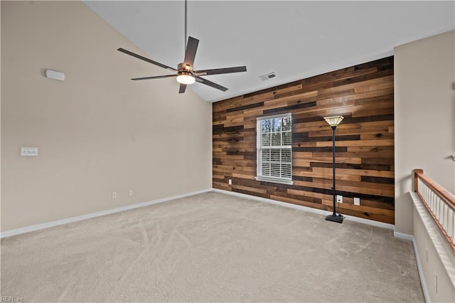 spare room with visible vents, carpet, wooden walls, baseboards, and ceiling fan