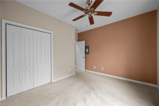 unfurnished bedroom featuring a ceiling fan, electric panel, a closet, baseboards, and light colored carpet