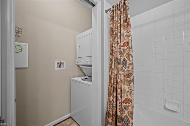 laundry area with tile patterned flooring, laundry area, baseboards, and stacked washing maching and dryer