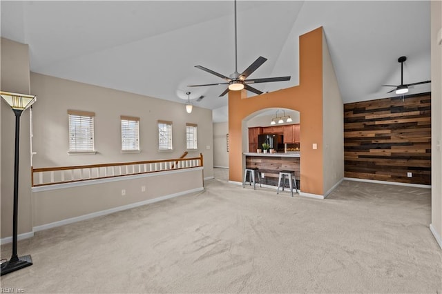 unfurnished living room featuring carpet floors, high vaulted ceiling, ceiling fan, wood walls, and an accent wall