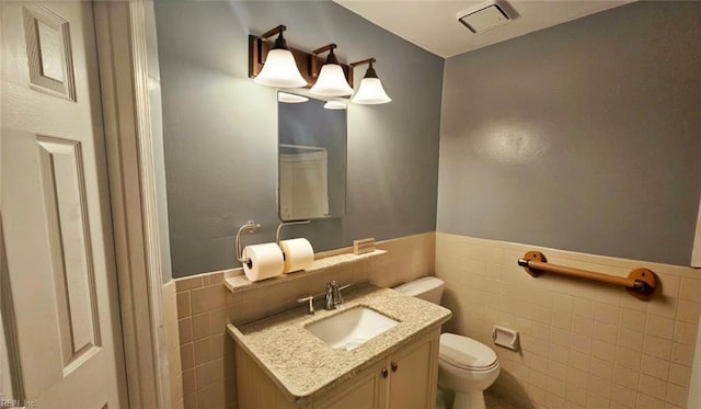 bathroom featuring wainscoting, vanity, toilet, and tile walls