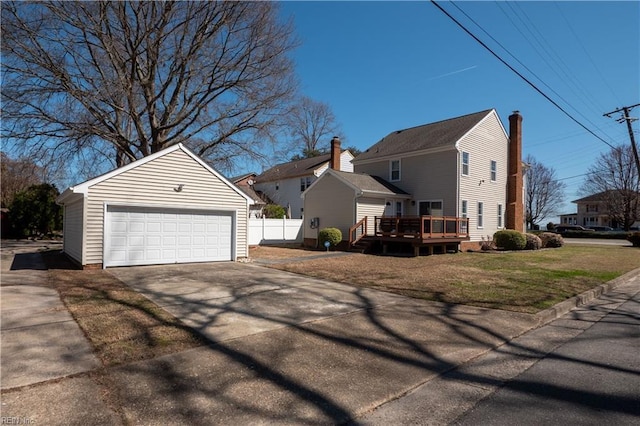 view of property exterior with a detached garage, fence, a lawn, a deck, and an outbuilding