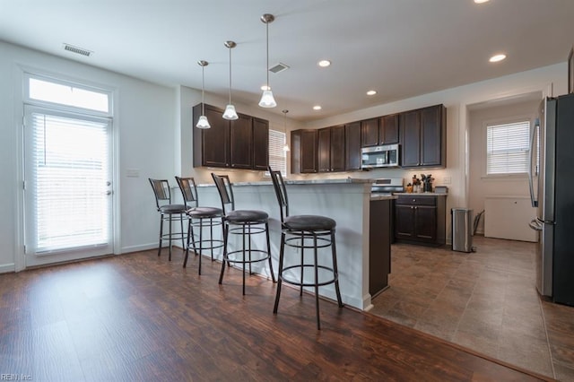 kitchen with a breakfast bar area, visible vents, a peninsula, stainless steel appliances, and dark brown cabinets