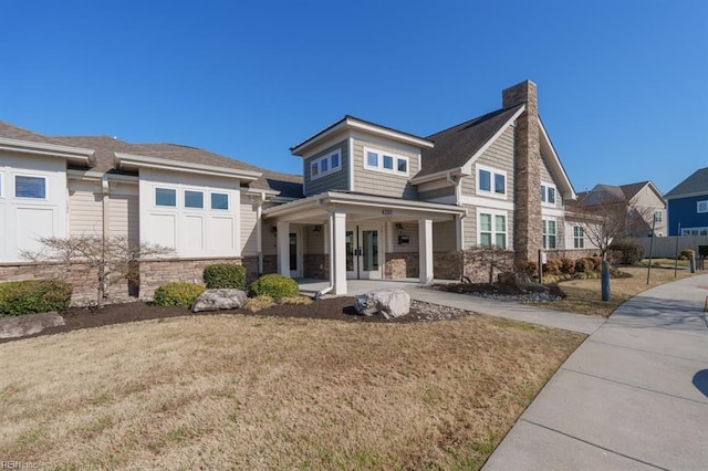 view of front of home featuring french doors, stone siding, a front lawn, and a chimney