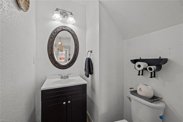 half bathroom featuring lofted ceiling, toilet, vanity, and a textured wall