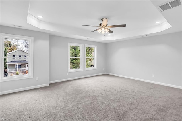 carpeted spare room with a wealth of natural light, visible vents, baseboards, and a tray ceiling