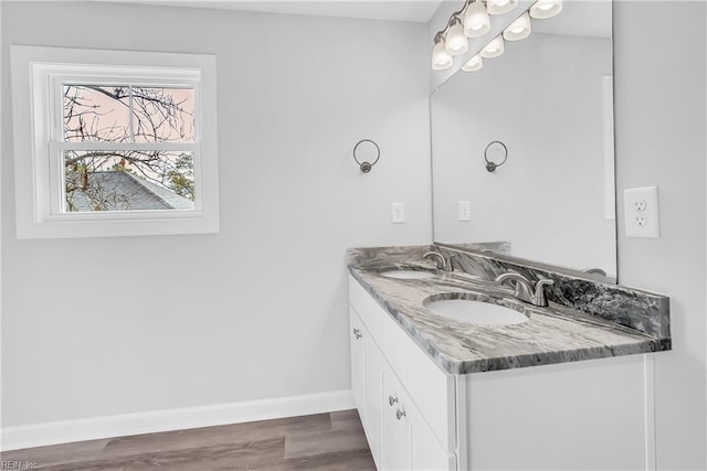 full bath with double vanity, wood finished floors, baseboards, and a sink