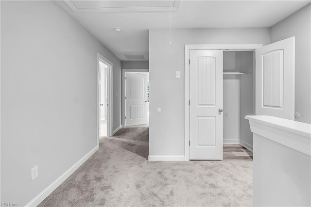 hallway featuring baseboards, carpet, and attic access