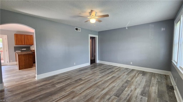 empty room featuring visible vents, baseboards, wood finished floors, arched walkways, and a textured ceiling