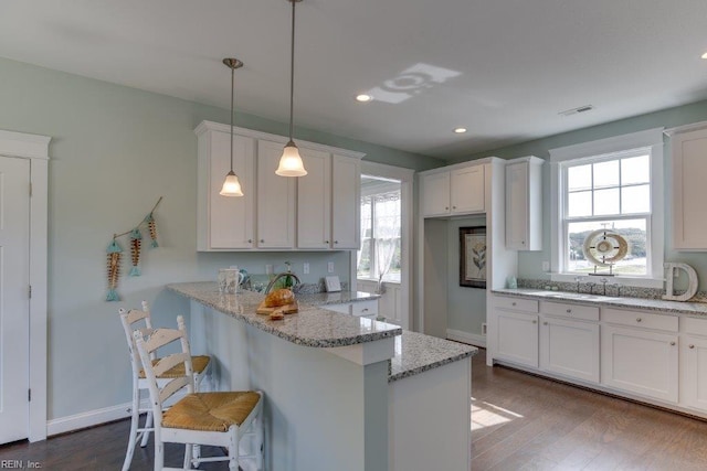 kitchen with light stone counters, a peninsula, white cabinetry, and dark wood-style flooring