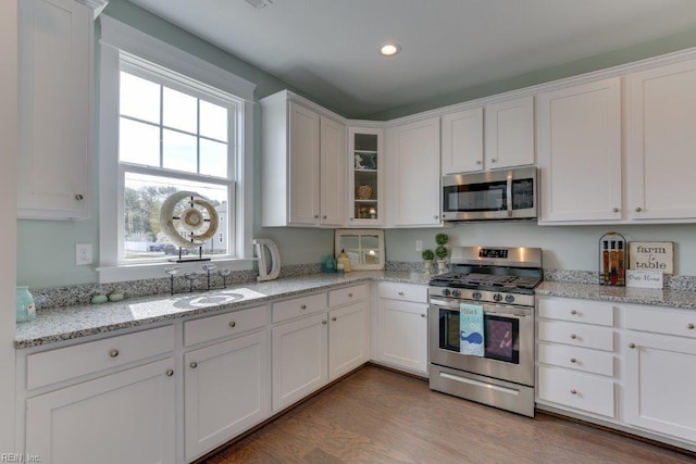 kitchen featuring a sink, wood finished floors, white cabinetry, appliances with stainless steel finishes, and glass insert cabinets