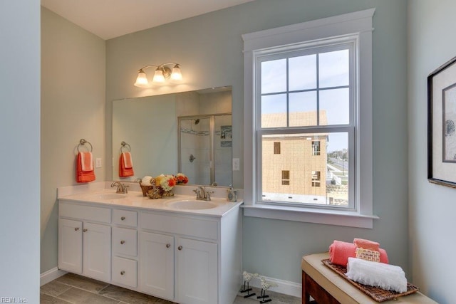 full bath with double vanity, a shower stall, baseboards, and a sink