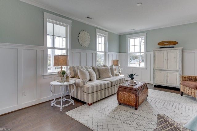 living room with visible vents, crown molding, a wainscoted wall, wood finished floors, and a decorative wall