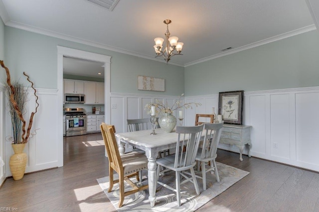 dining space featuring visible vents, a notable chandelier, wood finished floors, crown molding, and a decorative wall