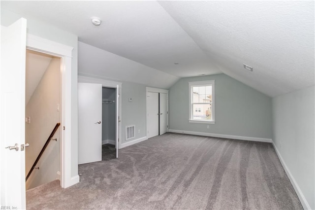 additional living space featuring baseboards, visible vents, carpet floors, vaulted ceiling, and a textured ceiling