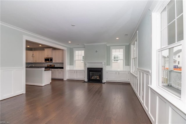 unfurnished living room with dark wood finished floors, a fireplace with flush hearth, wainscoting, and ornamental molding