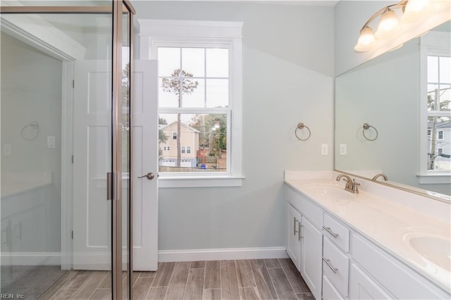 full bath featuring wood tiled floor, double vanity, baseboards, and a sink