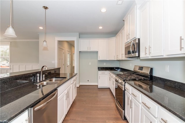 kitchen featuring decorative light fixtures, dark stone countertops, appliances with stainless steel finishes, white cabinets, and a sink