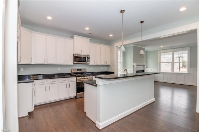 kitchen featuring dark wood-style flooring, white cabinets, appliances with stainless steel finishes, pendant lighting, and dark countertops