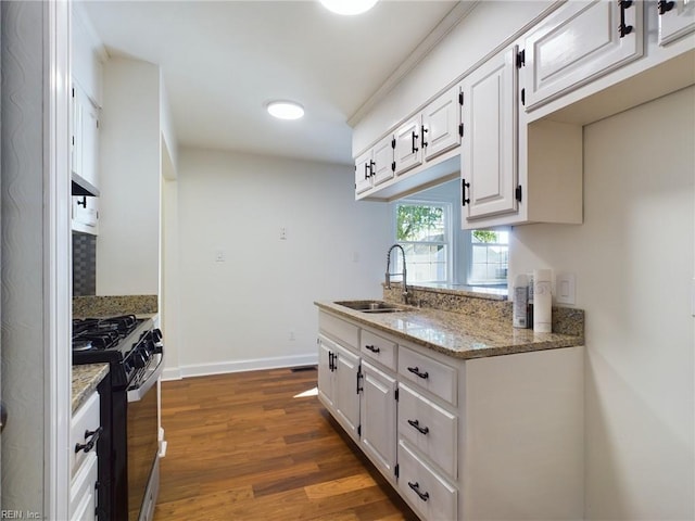 kitchen featuring dark wood-style floors, baseboards, black gas stove, a sink, and white cabinetry