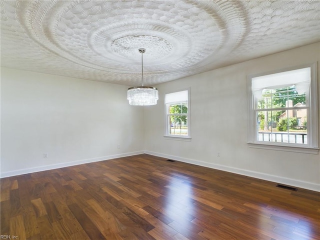 empty room with dark wood-style floors, a notable chandelier, baseboards, and a tray ceiling