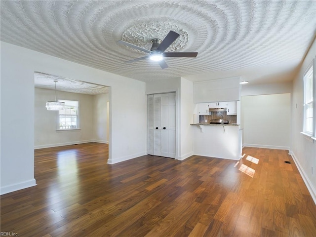 unfurnished living room featuring baseboards, a textured ceiling, dark wood-style floors, and a ceiling fan