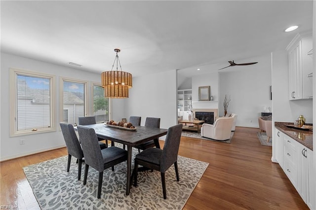 dining room featuring wood finished floors, baseboards, recessed lighting, a glass covered fireplace, and a notable chandelier