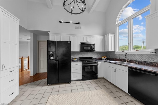 kitchen featuring dark countertops, light tile patterned floors, a high ceiling, black appliances, and a sink